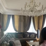 Espacio con mobiliario italiano de gran calidad, sofá suave, elegante mesa de centro, una lámpara majestuosa, cortinas refinadas, parquet impecable y apliques de pared de diseño